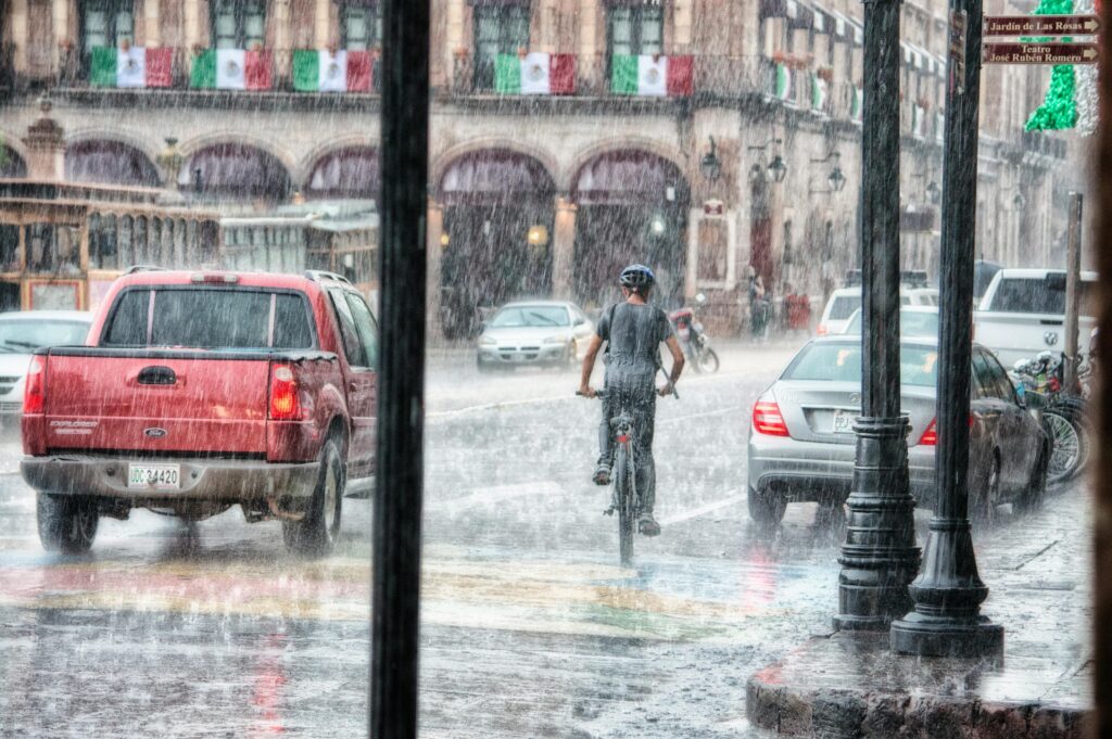 Pessoa andando de bicicleta no meio da rua com chuva de verão caindo